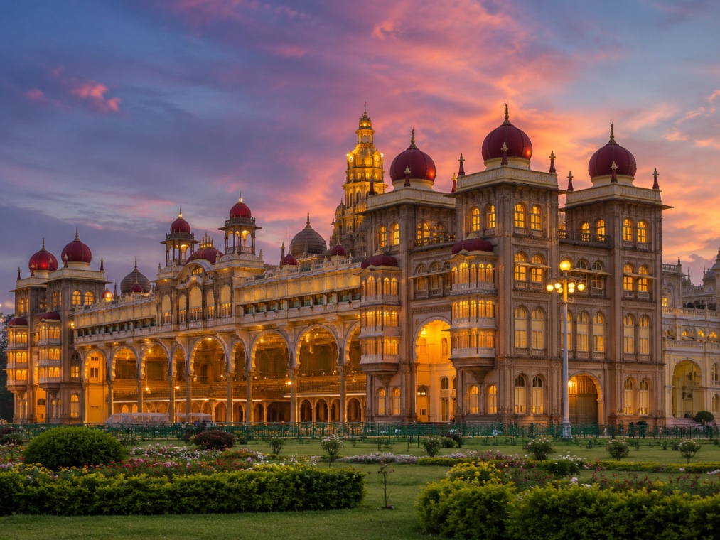 Mysore Palace illuminated at dusk, with its domed towers against a colorful evening sky